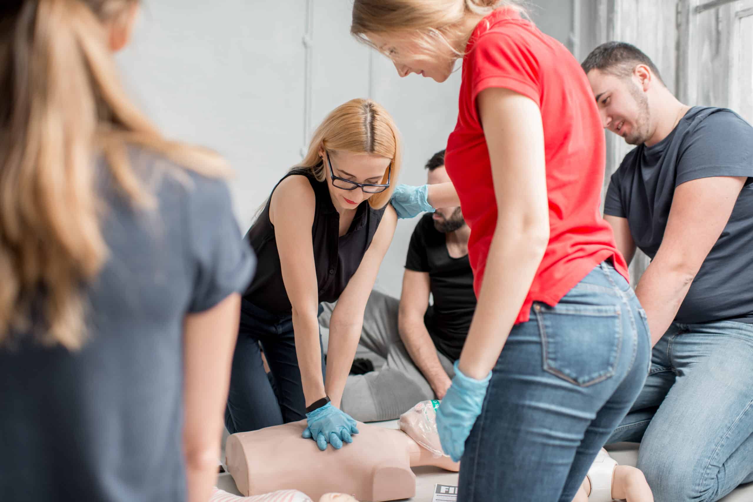 Group of people learning how to make first aid heart compressions with dummies during the training indoors
