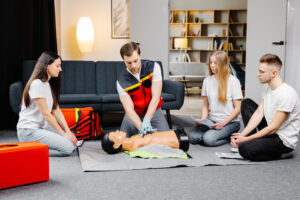 Young man instructor helping to make first aid heart compressions with dummy during the group training indoors. first aid renewal training