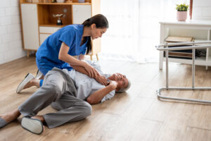 CPR renewal aged care - Asian caregiver helping senior male from falling on the ground at home. Elderly older patient having an accident after doing physical therapy then rescued by attractive therapist nurse in living room.