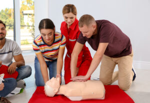 Group of people with instructor practicing CPR on mannequin at first aid class indoors CPR refresher