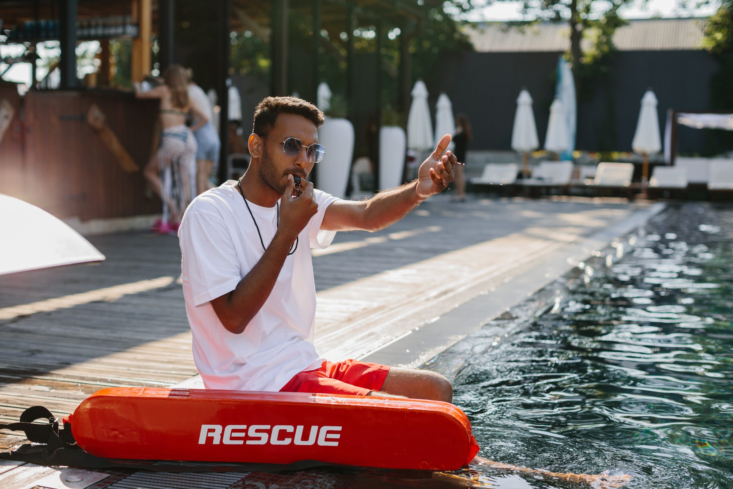 Pool Lifeguard blowing whistle and pointing at the poolside