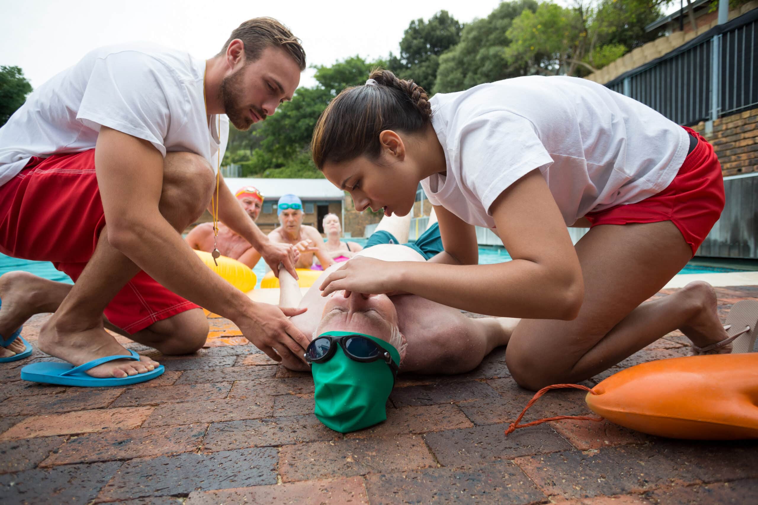 Male and female rescue workers helping unconscious senior man at poolside