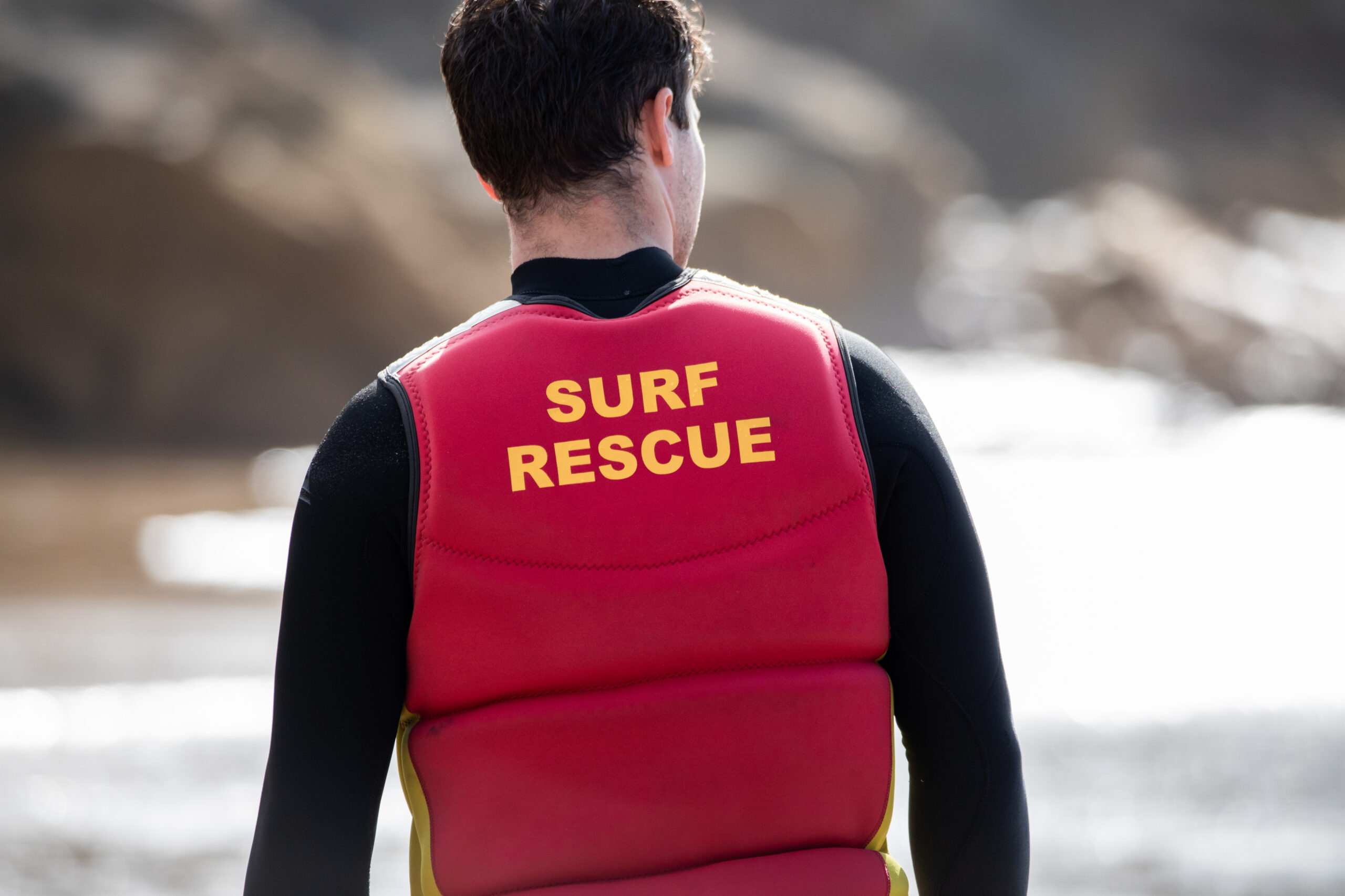 view from behind of male surf life saver patrolling beach.